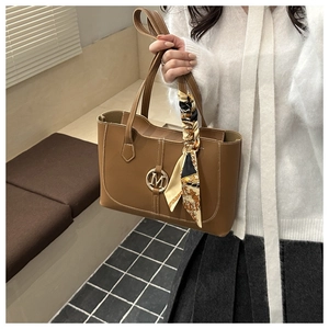 Close-up of brown leather tote bag with gold M-logo and printed silk scarf on handle