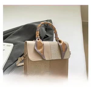 Detail of light beige crossbody bag with textured leather, woven fabric, and silk scarf