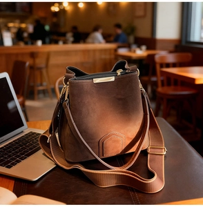 Detailed shot of brown suede bucket bag with gold hardware on a wooden coffee table