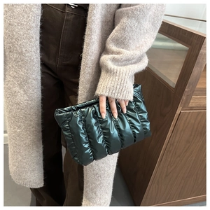 Close-up of a model holding a dark green quilted cloud clutch with glossy finish