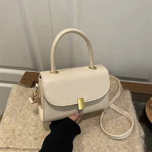 Minimalist beige leather handbag with gold buckle and top handle shown in a lifestyle setting