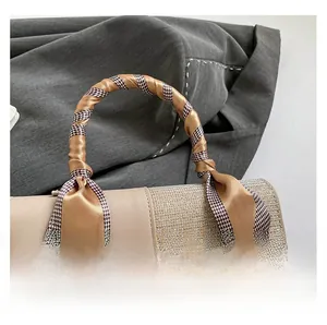 Detail of beige square bag featuring woven flap and silk scarf wrapped handle