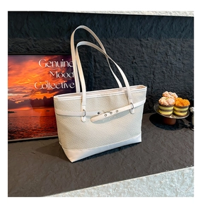 Detail of the woven texture and adjustable leather strap on a cream tote bag
