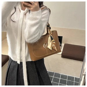 Close-up of brown tote bag with gold M buckle and elegant floral silk scarf handle