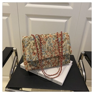 Detail einer floralen Brokat-Handtasche mit rot-goldener Kette auf einem Buch