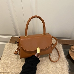 Vintage brown leather crossbody bag with top handle and gold clasp on soft fabric