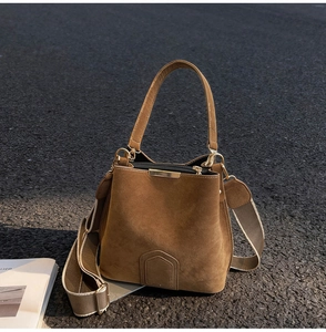 Detail of caramel suede bucket bag with striped fabric strap and gold hardware