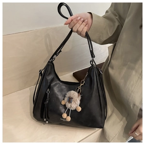 Detail der schwarzen PU-Ledertasche mit Plüschlamm-Anhänger und seitlicher Reißverschlusstasche