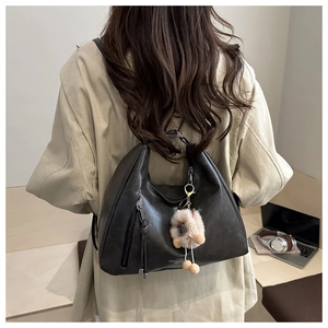 Detail der schwarzen Hobo-Tasche aus Leder mit Metallreißverschluss und Plüschtier-Anhänger