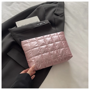 Vue détaillée d'une pochette en satin rose matelassé posée sur un blazer noir avec livre