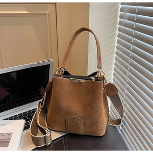 Close-up of brown suede bucket bag with wide woven strap and gold metal hardware detail