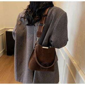 Detail of vintage brown suede bucket bag with wide strap and fine stitching on grey coat