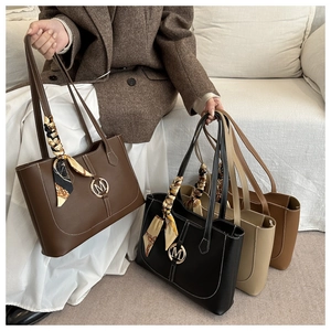 Detail of tote bag showing M logo hardware, contrast stitching, and silk scarf handle