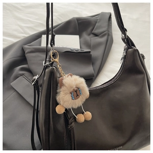 Detail eines hellbraunen Plüschpuppen-Anhängers mit goldenem Clip an brauner Ledertasche