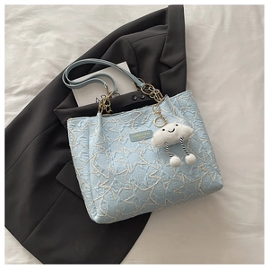 Détail d'un sac cabas bleu clair avec texture gaufrée et breloque nuage en peluche