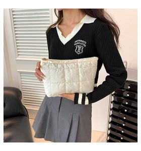 Détail d'une pochette matelassée ivoire en nylon avec zip doré tenue par un mannequin en scène