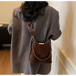 Close-up of a vintage brown suede bucket bag with wide strap and metallic hardware