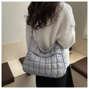 Vue détaillée du sac à bandoulière matelassé gris porté avec un pull blanc moderne