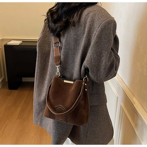 Detail of dark brown suede bucket bag featuring elegant gold metal bar and wide shoulder strap