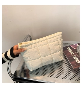 Détail d'une pochette en nylon matelassé blanc montrant le rembourrage et le zip doré