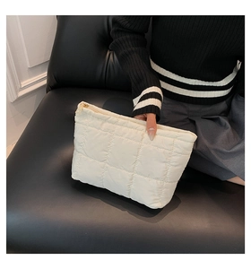 Détail de la pochette matelassée crème avec fermeture éclair dorée sur fond en cuir noir