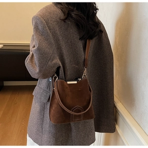 Detail of dark brown suede bucket bag featuring metallic top bar and refined stitching