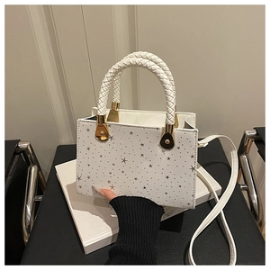 White square handbag with star-shaped cutouts and braided handle on a decorative book