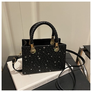 Detail of black tote bag with silver star prints and thick braided handle on a white book
