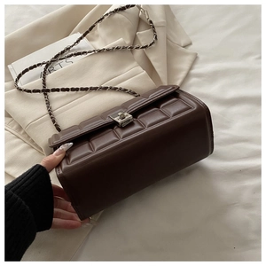 Detail of brown quilted crossbody bag with metal chain strap and twist lock on blazer