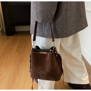 Detail view of brown suede bucket bag with gold hardware and a slim shoulder strap
