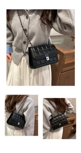 Detail of a black quilted leather crossbody bag with silver chain and metal turn-lock clasp