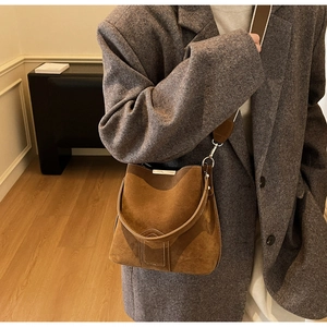 Close-up of retro brown suede bucket bag with wide strap on grey oversized blazer