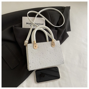Detailed view of white square bag with star patterns beside a smartphone for size reference