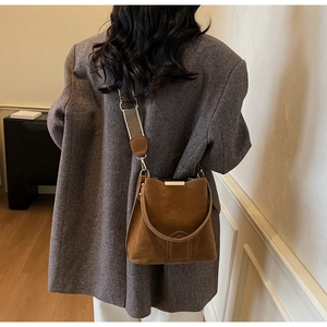 Brown suede bucket bag detail with colorful woven strap on a model wearing wool blazer