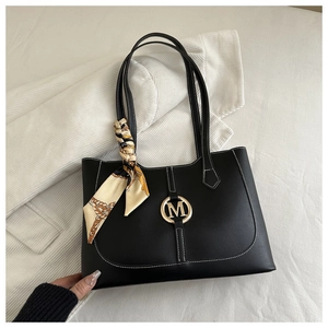 Detail of black faux leather tote bag with white stitching and gold M hardware accent