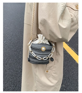 Detail of woven bucket bag with pearl embellishments and gold chain strap in outdoor setting