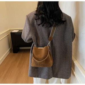 Detail of vintage brown suede bucket bag with striped wide shoulder strap worn by a model