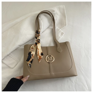 Detail of a brown leather tote bag with a golden M buckle and a silk scarf on the handle