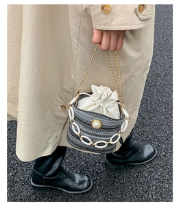 Chic woven bucket bag with elegant pearl detail and gold chain handle held by a model
