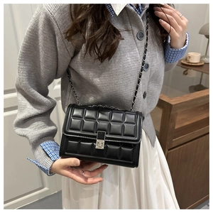 Close-up of quilted black crossbody bag with metal chain strap and turn-lock closure