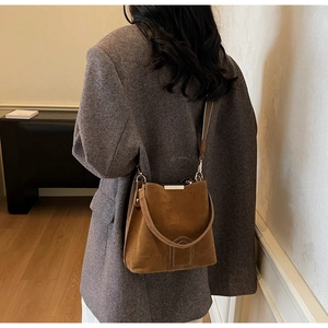 Brown suede bucket bag detail showing the golden metal trim and sleek shoulder strap