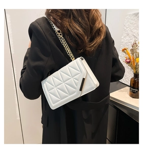 Close-up of white quilted handbag with gold chain strap on a black blazer