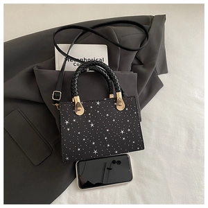 Close-up of small black square handbag with star print next to a phone for size reference