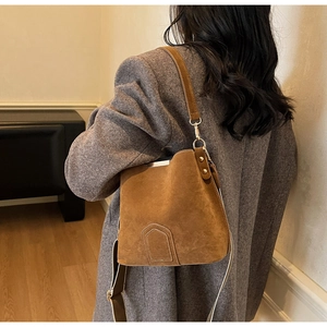Detailed view of brown suede bucket bag featuring metal trim and dual textured straps