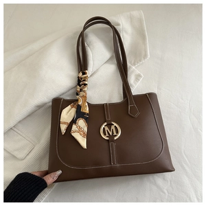 Detail of brown tote bag featuring white stitching, golden M buckle and silk scarf handle