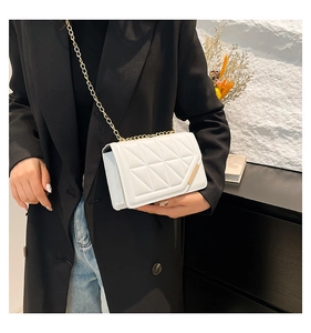 Detail view of a white quilted crossbody bag with gold chain strap worn by a model