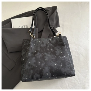 Detail of moon and star print on a black tote bag with elegant gold metal ring connectors