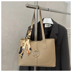 Close-up of beige tote bag featuring metal M-logo and decorative silk scarf detail