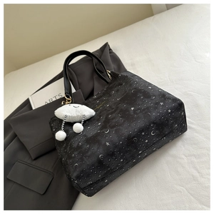 Detailed view of black star and moon tote bag with a white plush cloud charm accessory