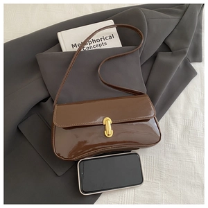 Detail view of brown patent leather underarm bag with gold buckle next to a smartphone for size
